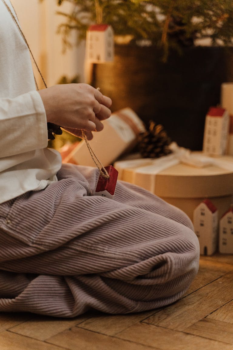 Child kneeling near Christmas tree, holding a festive ornament amidst gifts.
